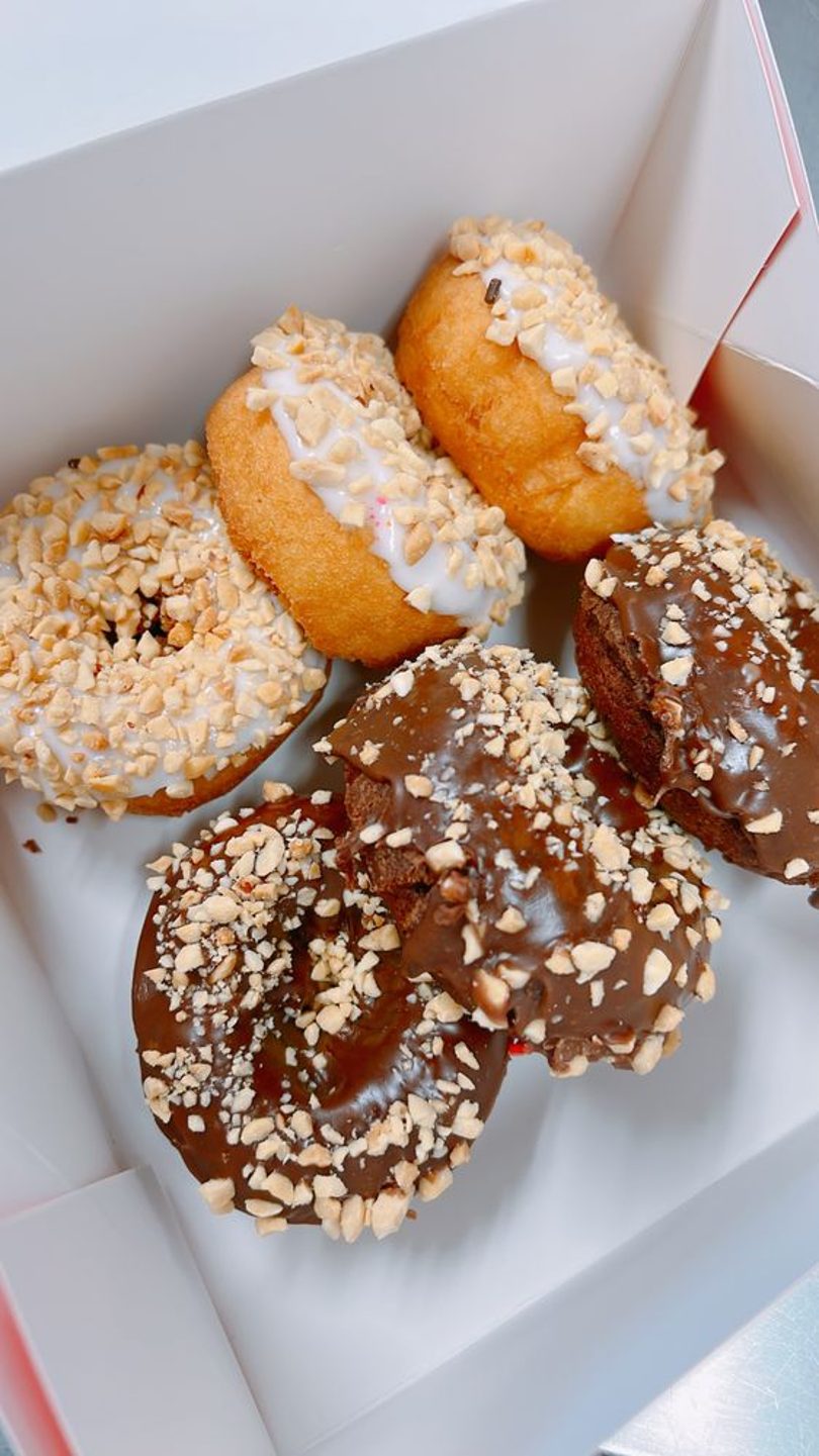 A box of chocolate and glazed donuts topped with chopped peanuts.