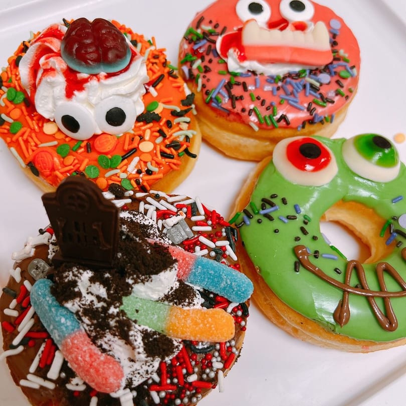 Four Halloween monster donuts with candy eyes, fangs, and colorful sprinkles.