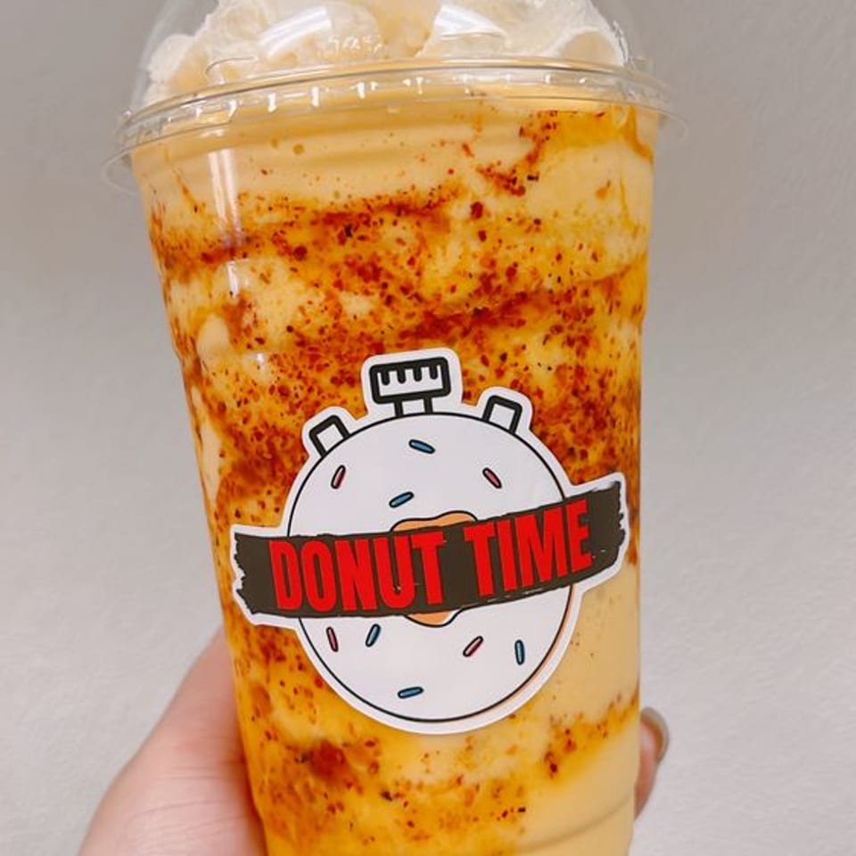 A Donut Time iced Vietnamese coffee topped with whipped cream, held in hand.