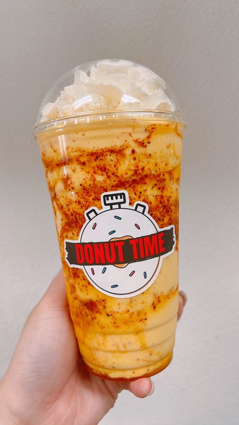 A Donut Time iced Vietnamese coffee topped with whipped cream, held in hand.