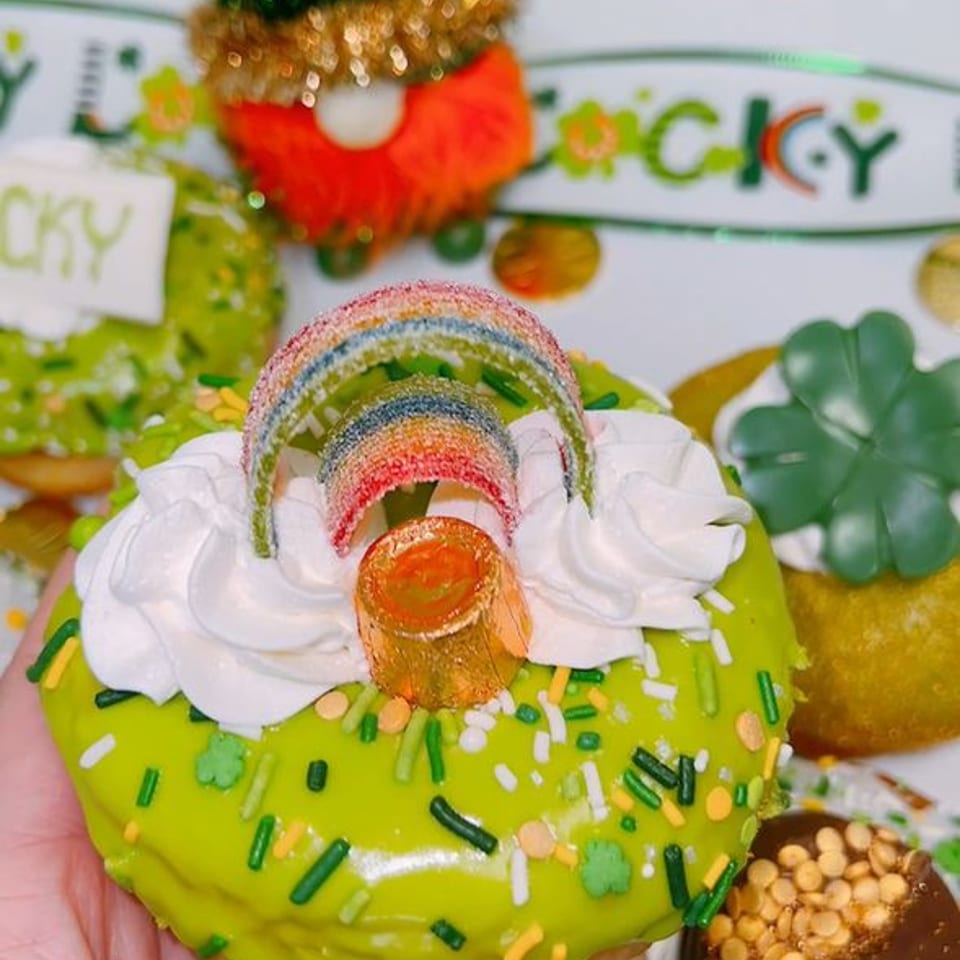 A green St. Patrick's Day donut with a rainbow candy topper, held in hand.