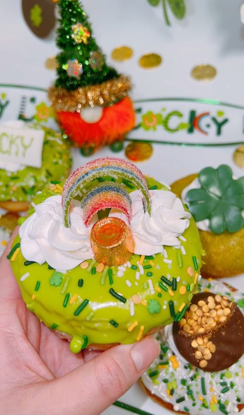 A green St. Patrick's Day donut with a rainbow candy topper, held in hand.