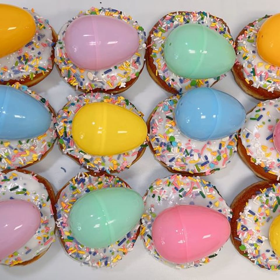 White-frosted Easter donuts with pastel sprinkles and plastic egg toppers.