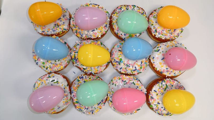 White-frosted Easter donuts with pastel sprinkles and plastic egg toppers.